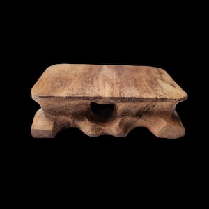 May include: A small, wooden, rectangular stand with a carved, wavy base and a heart-shaped cutout in the center. The stand is made of dark brown wood and has a natural, rustic finish.