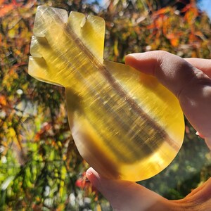 May include: A yellow fluorite crystal carved into the shape of an arrow. The crystal is translucent and has a striated pattern.