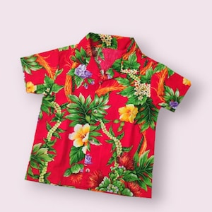 May include: Red short-sleeved shirt with a tropical floral print. The shirt features a variety of flowers, leaves, and a red and yellow flower with a white center.