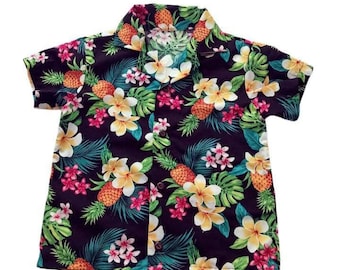 Puede incluir: Una camisa de manga corta con botones y estampado tropical con piñas, flores y hojas sobre un fondo morado oscuro.