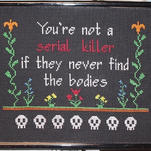 May include: Black framed cross-stitch with the text "You're not a serial killer if they never find the bodies" and five white skull images at the bottom.