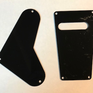 May include: Two black plastic guitar pickguards. One is shaped like a teardrop and the other is rectangular with a cutout for a pickup.