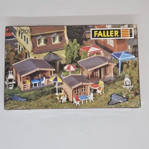May include: A model kit of a small village scene with three wooden houses, a barbecue, a pond, and several trees. The kit is made by Faller and is labelled with the number 2209.