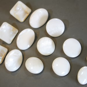 Puede incluir: Surtido de botones de nácar de color blanco y crema en varias formas y tamaños. Los botones son lisos y brillantes.