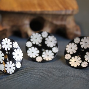May include: Three black and white rings with a floral design. The rings are made of metal and have a shiny finish.