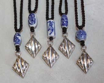 May include: Six silver pendants with a diamond shape and a textured surface hang from black cords. Each pendant is attached to a blue and white porcelain bead with Chinese characters.