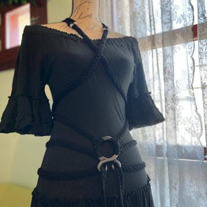 May include: A black off-the-shoulder dress with a rope belt featuring a large silver ring. The dress has a ruffled hem and short sleeves.