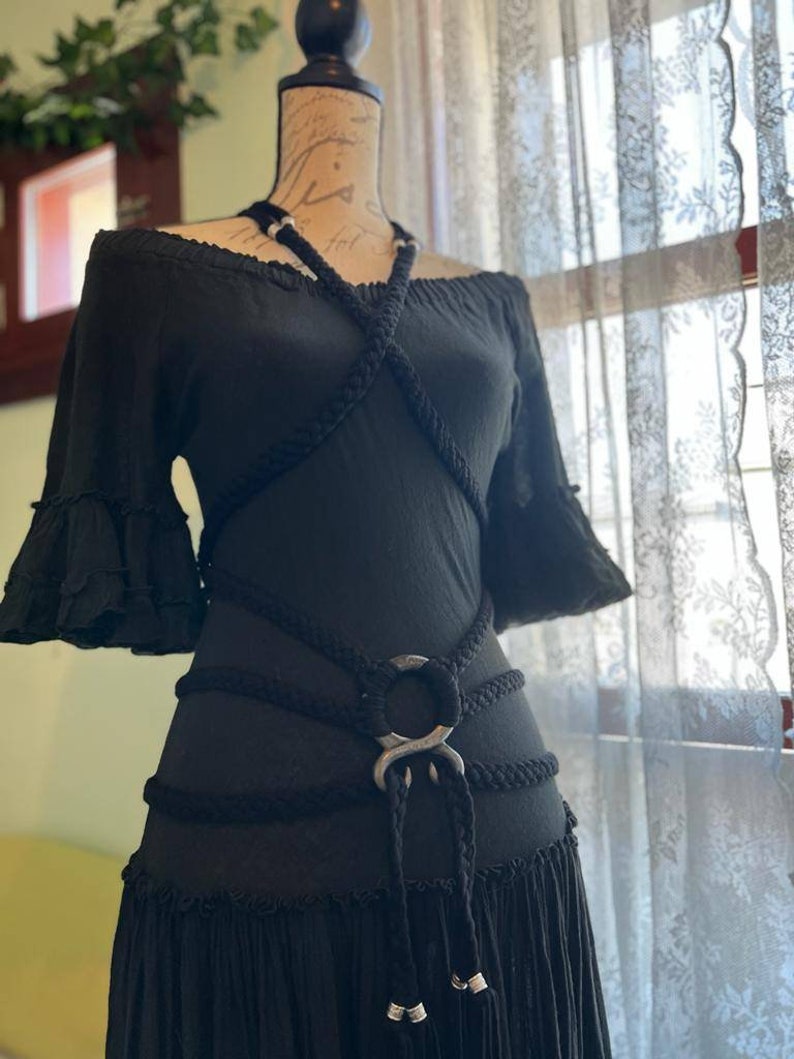 May include: A black off-the-shoulder dress with a rope belt featuring a large silver ring. The dress has a ruffled hem and short sleeves.