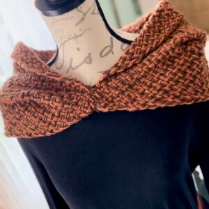 May include: A brown knitted scarf with a textured pattern. The scarf is draped over a black long-sleeved shirt.