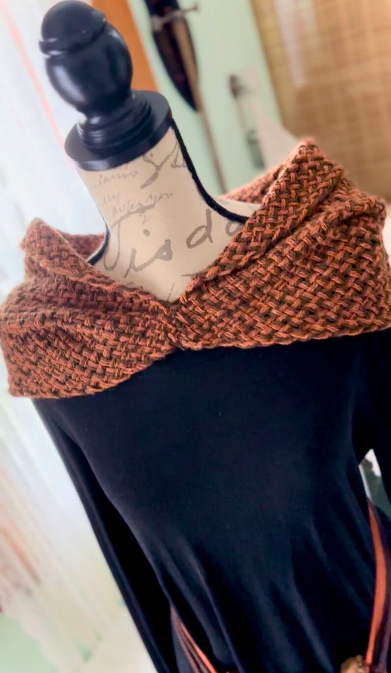 May include: A brown knitted scarf with a textured pattern. The scarf is draped over a black long-sleeved shirt.
