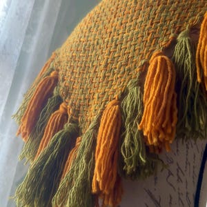 May include: A woven throw blanket with a green and orange pattern and fringe tassels.