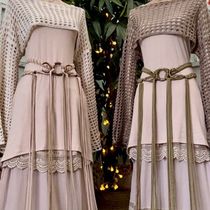 May include: Two long, flowy dresses with crochet tops and layered lace trim. Both dresses feature a brown leather belt with a large metal ring and tassels.