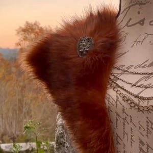 May include: A brown faux fur shawl with a decorative metal brooch. The shawl is draped over a mannequin with a handwritten note on the fabric.
