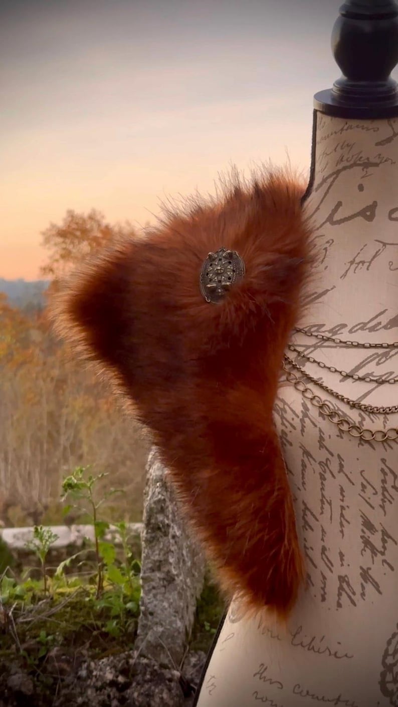 May include: A brown faux fur shawl with a decorative metal brooch. The shawl is draped over a mannequin with a handwritten note on the fabric.