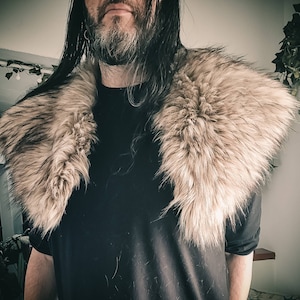 K&ouml;nnte beinhalten: Eine Person tr&auml;gt ein schwarzes Hemd mit einem gro&szlig;en, flauschigen, hellbraunen Pelzkragen.