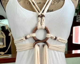 May include: A white fabric body harness with a large copper ring and smaller copper beads. The harness is tied in a criss-cross pattern across the chest and waist.