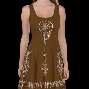 K&ouml;nnte beinhalten: Ein braunes, &auml;rmelloses Kleid mit einem wei&szlig;en Design aus Kompass und Runen. Das Kleid hat einen ausgestellten Rock und einen wei&szlig;en Band aus Runen am Saum.