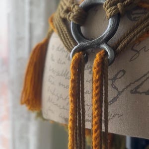 May include: A brown and orange braided belt with a large silver ring buckle. The belt is tied with long tassels.