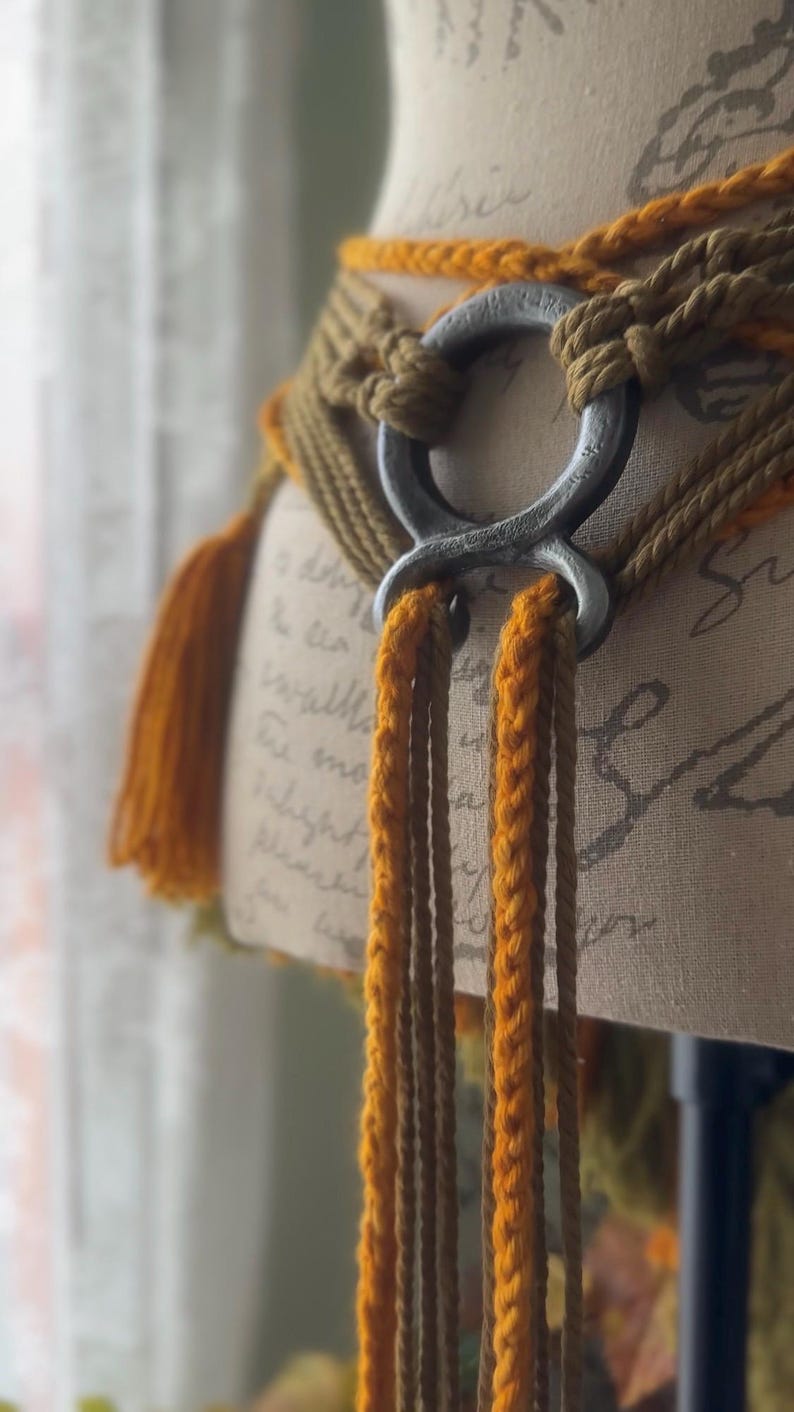 May include: A brown and orange braided belt with a large silver ring buckle. The belt is tied with long tassels.
