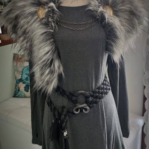 May include: A gray long-sleeved tunic with a faux fur collar and a black braided belt with a silver buckle. The collar has two gold buttons.