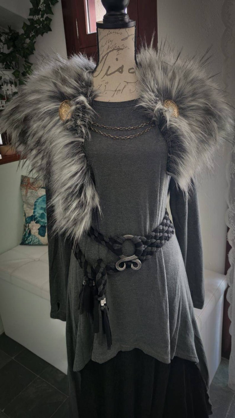 May include: A gray long-sleeved tunic with a faux fur collar and a black braided belt with a silver buckle. The collar has two gold buttons.