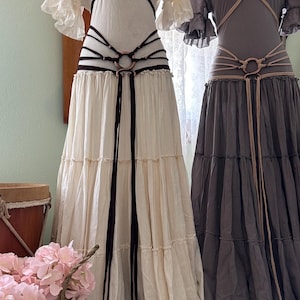May include: Two white and gray maxi dresses with brown and beige leather belts with metal rings. The dresses have a tiered skirt and a ruffled neckline.