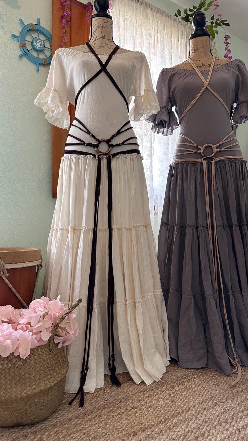 May include: Two white and gray maxi dresses with brown and beige leather belts with metal rings. The dresses have a tiered skirt and a ruffled neckline.