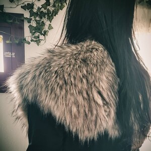 K&ouml;nnte beinhalten: Eine schwarze Jacke mit einem gro&szlig;en, flauschigen, grauen Pelzkragen. Das Fell ist weich und scheint aus Kunstfell zu sein.