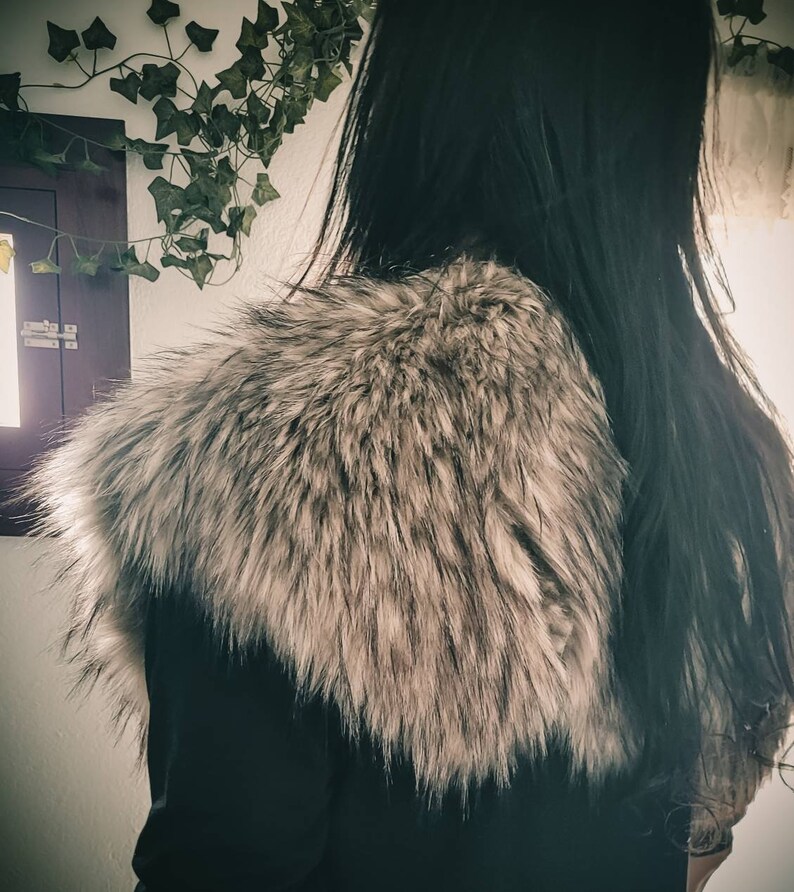 K&ouml;nnte beinhalten: Eine schwarze Jacke mit einem gro&szlig;en, flauschigen, grauen Pelzkragen. Das Fell ist weich und scheint aus Kunstfell zu sein.