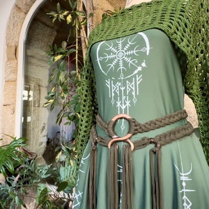 K&ouml;nnte beinhalten: Ein gr&uuml;nes Kleid mit einem wei&szlig;en Design eines Kreises mit einem Schneeflocke darin und Runen darum herum. Das Kleid hat einen gr&uuml;nen H&auml;kel-Schal und einen geflochtenen gr&uuml;nen G&uuml;rtel mit einem gro&szlig;en Metallring.