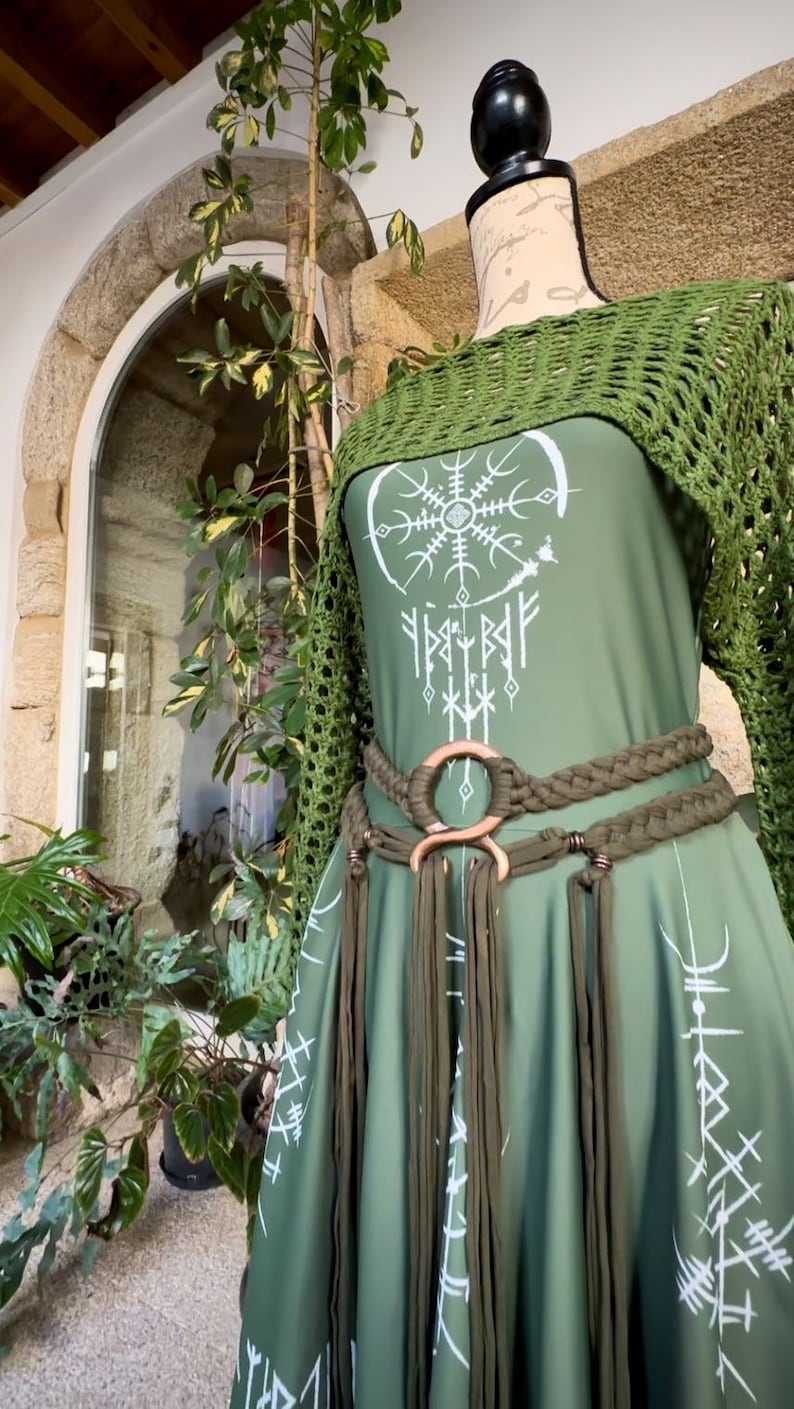 K&ouml;nnte beinhalten: Ein gr&uuml;nes Kleid mit einem wei&szlig;en Design eines Kreises mit einem Schneeflocke darin und Runen darum herum. Das Kleid hat einen gr&uuml;nen H&auml;kel-Schal und einen geflochtenen gr&uuml;nen G&uuml;rtel mit einem gro&szlig;en Metallring.