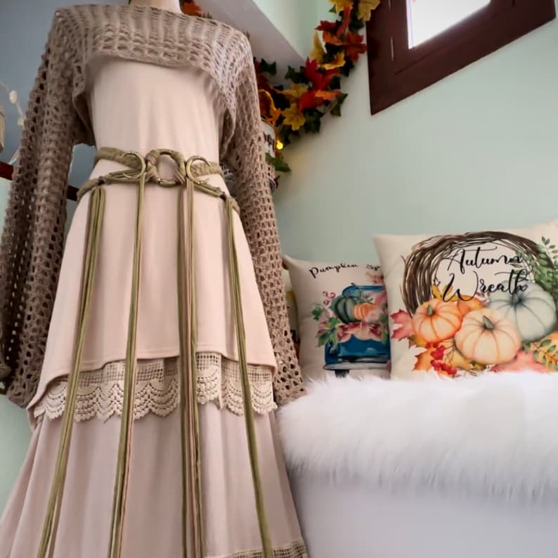 May include: A long, flowing beige skirt with a crocheted top and a brown leather belt with tassels. The skirt has a lace trim and the top has long sleeves. The skirt is paired with a brown crocheted top and a brown leather belt with tassels.