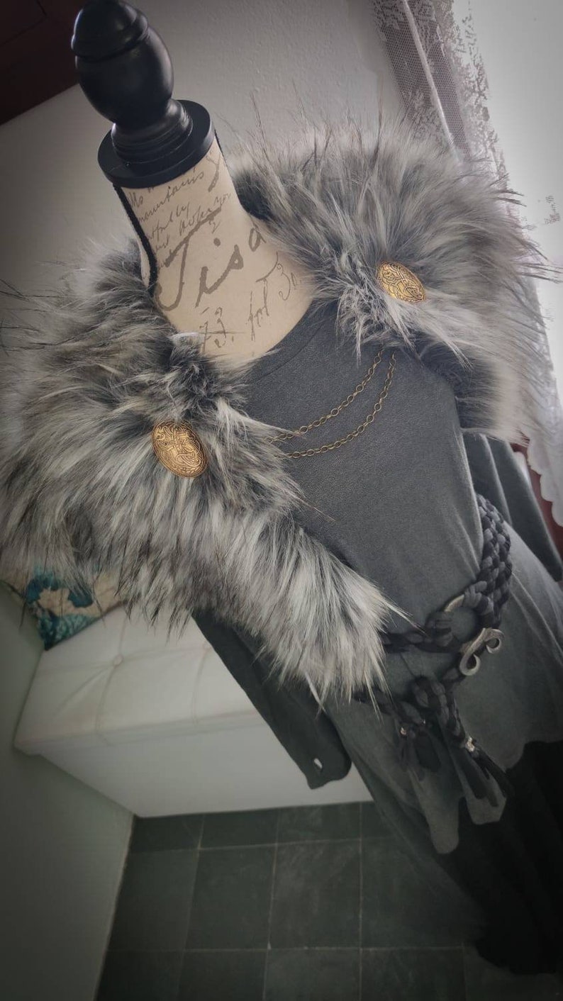 May include: A gray fur collar with two gold buttons and a chain necklace. The collar is worn over a gray long-sleeved shirt with a black belt.