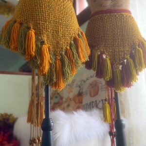 May include: Two crocheted skirts with fringe, one in shades of green and yellow, the other in shades of red and yellow. The skirts are displayed on mannequins.