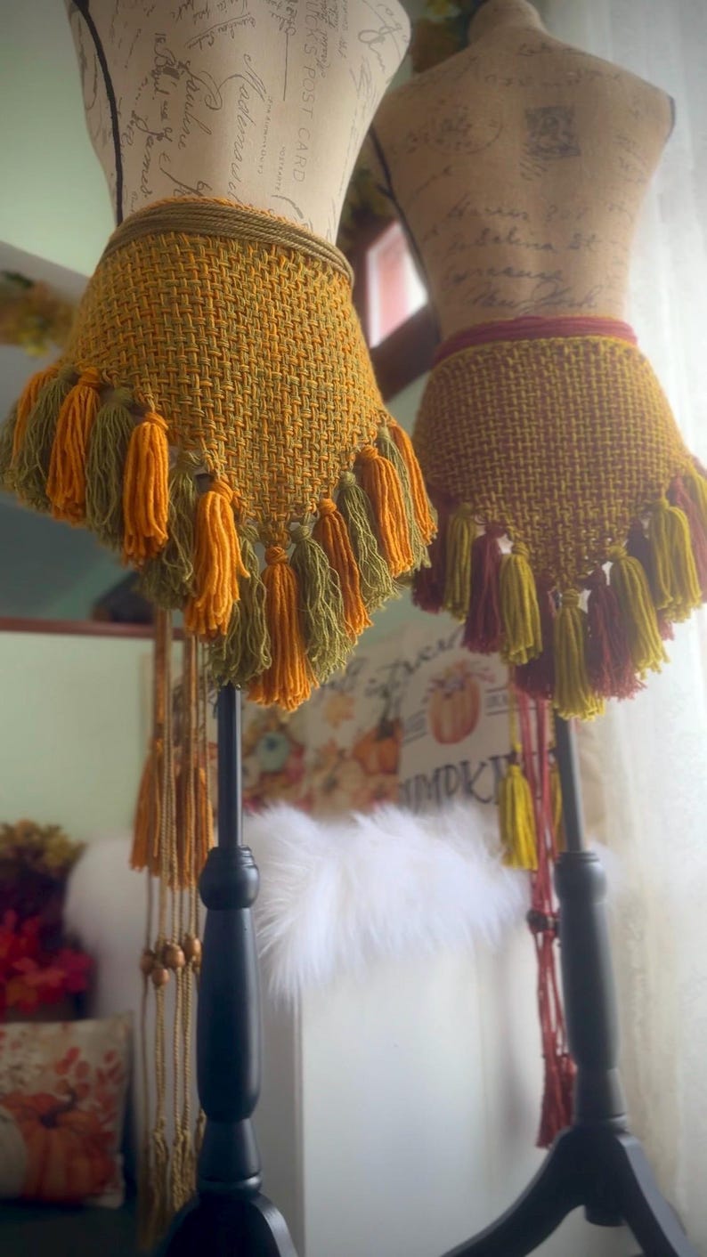 May include: Two crocheted skirts with fringe, one in shades of green and yellow, the other in shades of red and yellow. The skirts are displayed on mannequins.
