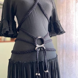 May include: A black off-the-shoulder dress with a thick black rope belt featuring a silver metal ring and tassels.