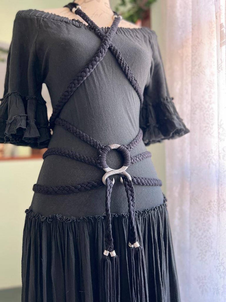 May include: A black off-the-shoulder dress with a thick black rope belt featuring a silver metal ring and tassels.