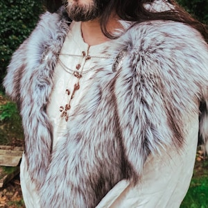 May include: A white fur collar with silver metal clasps. The collar is worn over a white shirt with a lace-up front.