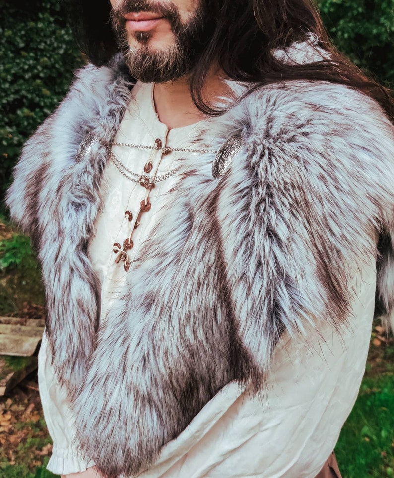 May include: A white fur collar with silver metal clasps. The collar is worn over a white shirt with a lace-up front.