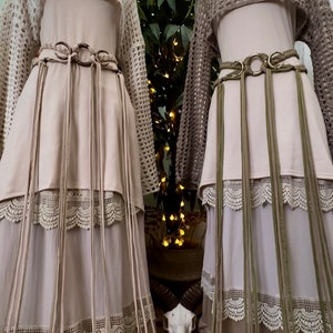 May include: Two long, flowing skirts with lace trim and fringe details. The skirts are layered and have a bohemian style. One skirt is beige and the other is green.