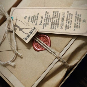 K&ouml;nnte beinhalten: Ein braunes Papierpaket, das mit Schnur gebunden und mit einem roten Wachssiegel versiegelt ist. Das Paket ist mit "Tribalwitch Designs" beschriftet und enth&auml;lt Pflegehinweise f&uuml;r ein Haarst&uuml;ck.