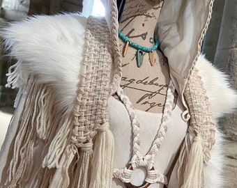 May include: Cream-colored hooded cloak with a faux fur collar and woven accents. The cloak features long fringe and a macrame-style bodice. A matching headband and turquoise and wooden bead necklace complete the ensemble.