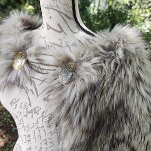 May include: A faux fur shawl with a brown and white color scheme. The shawl has two decorative metal clasps with intricate designs.