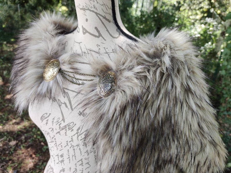 May include: A faux fur shawl with a brown and white color scheme. The shawl has two decorative metal clasps with intricate designs.