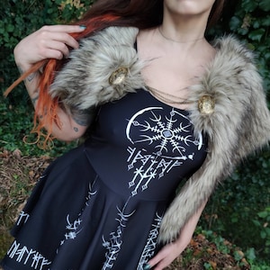 May include: A black dress with a white design of a circle with a star inside and runes around it. The dress has a fur collar with two gold buttons.
