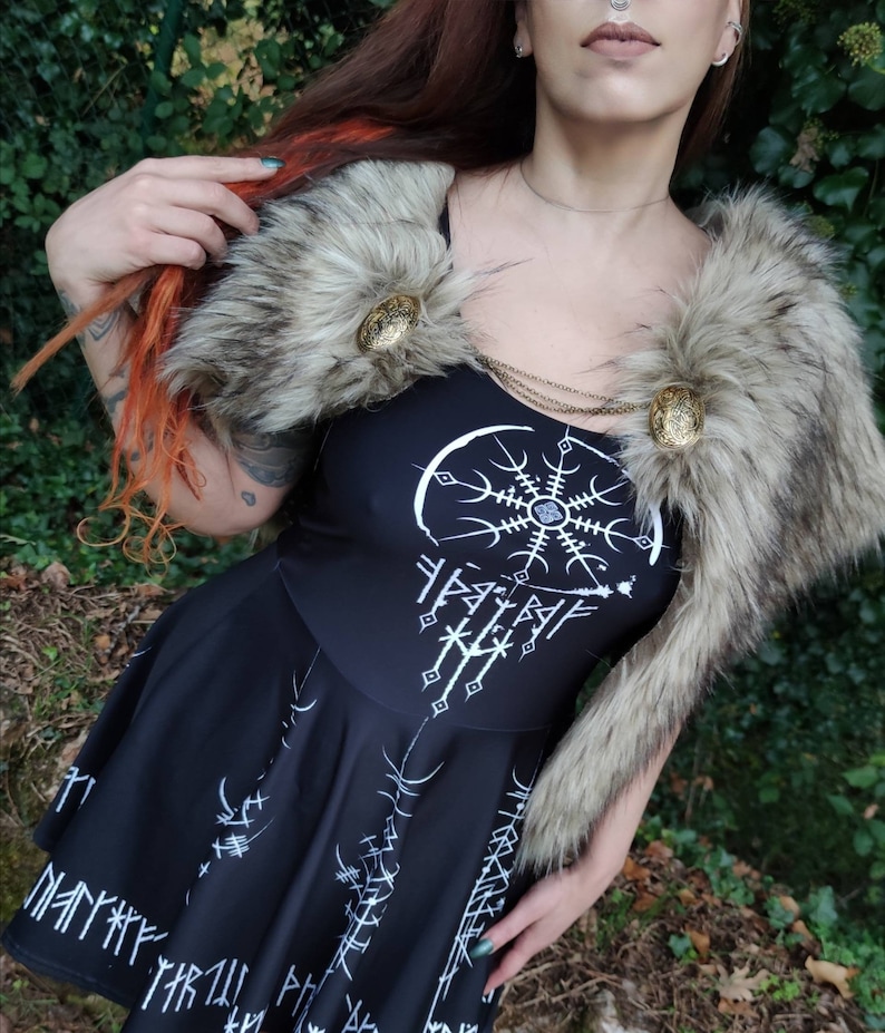May include: A black dress with a white design of a circle with a star inside and runes around it. The dress has a fur collar with two gold buttons.