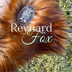May include: A close-up of a red fox fur tail with a silver decorative pin. The pin has a starburst design and the text "Reynard Fox" is written in green cursive.