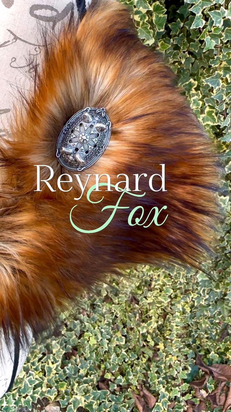 May include: A close-up of a red fox fur tail with a silver decorative pin. The pin has a starburst design and the text "Reynard Fox" is written in green cursive.
