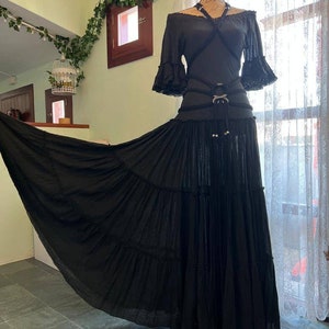 May include: A black off-the-shoulder top with a criss-cross design and a black skirt with multiple layers. The skirt is flowing and has a long train.