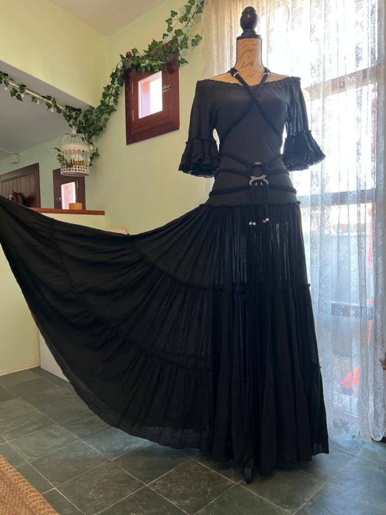 May include: A black off-the-shoulder top with a criss-cross design and a black skirt with multiple layers. The skirt is flowing and has a long train.